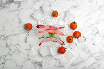 Frozen vegetables and ice cubes on marble table, top view
