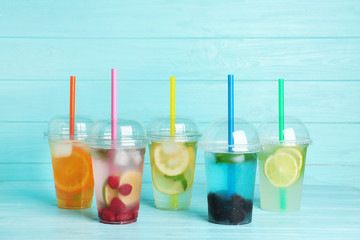 Plastic cups with lemonades on table against color background