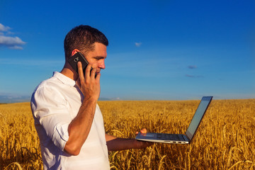 Naklejka na ściany i meble Young successful businessman is working in the middle of a field with a laptop. Freedom. A freelancer concept that works wherever it wants