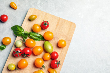 Wooden board with juicy tomatoes on grey background, top view