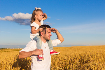 Happy family. Dad and daughter sitting on his shoulders stand in the middle of a wheat field on a sunny summer day