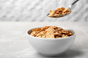 Spoon with cornflakes over bowl on table. Whole grain cereal
