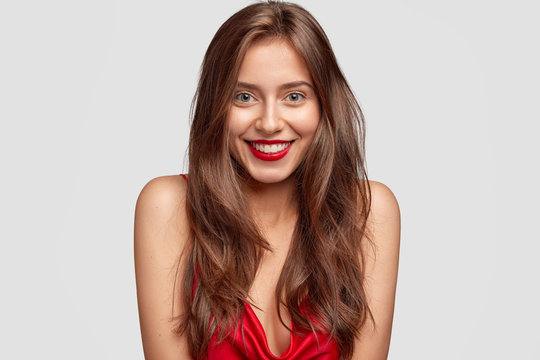 Beauty, fashion, makeup and people concept. Lovely happy woman with red lipstick, shows white perfect teeth, has healthy skin, long dark hair, isolated over white background, expresses happiness
