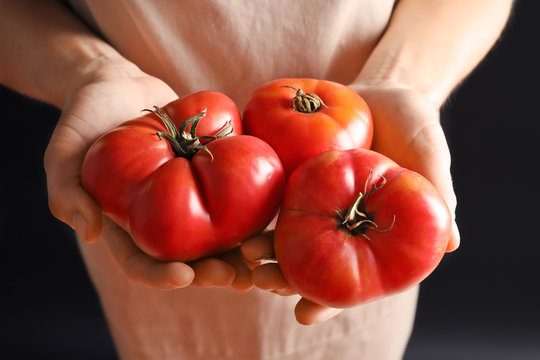 Woman holding tasty juicy tomatoes on black background, closeup
