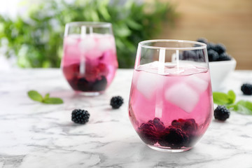 Glasses with iced blackberry lemonade on table against blurred background