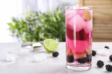Glass with iced blackberry lemonade on table against blurred background