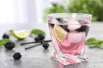 Glass with iced blackberry lemonade on grey table