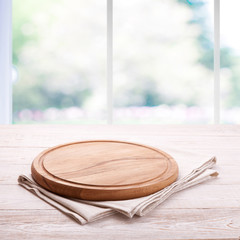 Board for pizza and tablecloth on empty wooden table near the window in kitchen. Canvas, dish...