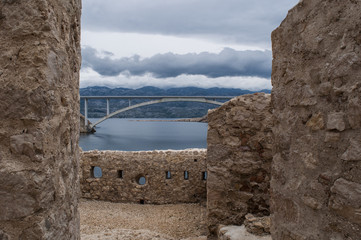 Fototapeta na wymiar Croazia: vista panoramica delle rovine di una torre di guardia e del Paški Most, il ponte del 1968 che collega la Croazia con l'isola di Pago, la quinta isola più grande della costa croata