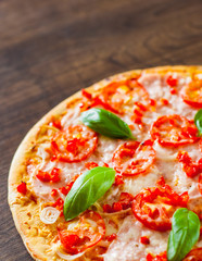 Pizza with Mozzarella cheese, Ham, Tomatoes, pepper, Spices and Fresh Basil. Italian pizza on wooden background.