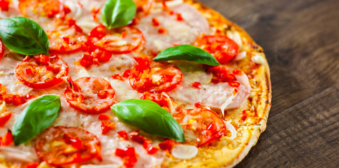 Pizza with Mozzarella cheese, Ham, Tomatoes, pepper, Spices and Fresh Basil. Italian pizza on wooden background.