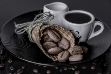 Breakfast. The waffle horn is filled with cookies on a black plate next to a cup of coffee and milk. Black background, close-up.