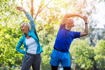 Happy fit senior couple exercising in park. - obrazy, fototapety, plakaty