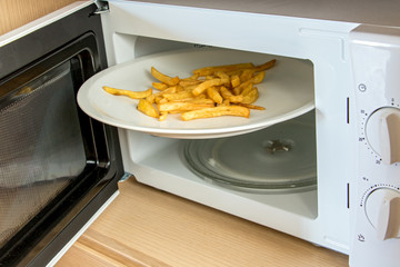 an open microwave with a white plate and roasted potatos. An large disc with french fries is wedged...