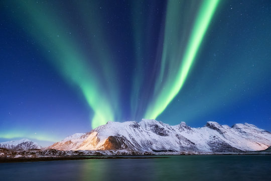 Aurora borealis on the Lofoten islands, Norway. Green northern lights above mountains. Night sky with polar lights. Night winter landscape with aurora and reflection on the water surface.