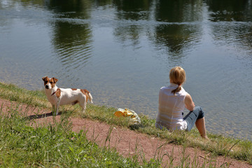Girl with blond hair sitting with a dog on the lake
