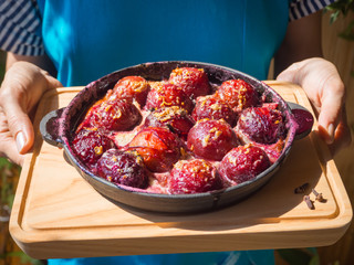 Dessert of baked plum in a pan with cloves, cinnamon, honey and zest.