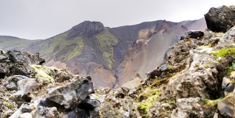 Obraz premium Moss-Covered Lava Rocks Framing Colorful Rhyolite Mountain Slopes in the Rainbow Mountains, Iceland