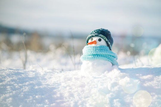 Little snowman in a cap and a scarf on snow in the winter. Christmas card with a lovely snowman, copy space