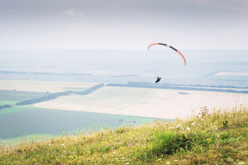 White orange paraglide with a paraglider in a cocoon against the background of fields of the sky and clouds. Paragliding Sports