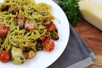 Pesto linguine with tomatoes, shrimps, and mussels on a white plate. 