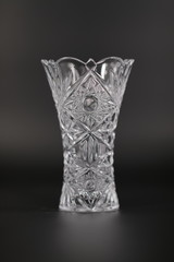 Carved vase from transparent material for flowers against a dark background.