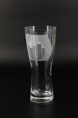 Tall glass from transparent glass for beer with the drawing put a stroke, against a dark background.