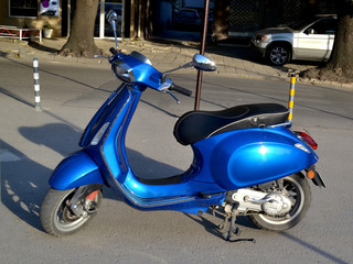 Bright blue colored scooter parked on the street on a summer day close-up
