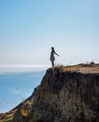 The girl is standing on a cliff near the sea.