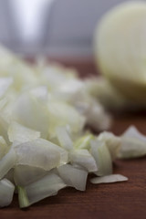 Pieces of chopped onions on the background of half an onion, close-up, vertical frame, wooden background.