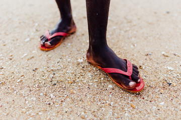 Feet of a Black Man in Red Flip Flops Standing on Sandy Beach