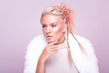 Gorgeous young woman in elegant winter fur coat, wearing makeup and braided hairstyle, posing against pink background. Studio lighting, retouched