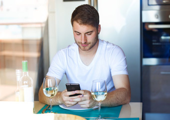 Handsome young man using his mobile phone in the kitchen at home.