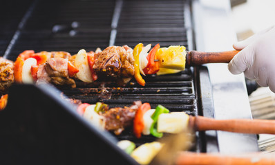 colorful barbecue stick on charcoal stove with chef's hand wearing glove holding wooden handle