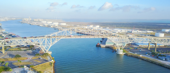 Panorama aerial view of Corpus Christi Harbor Bridge with row of oil tanks and wind turbines farm in distance. A through arch bridge crosses the Corpus Christi Ship Channel