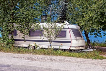 old gray residential container with windows in the grass and trees near the road