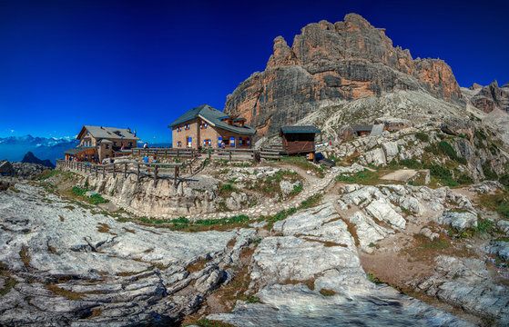 Beautiful view of Tuckett Refuge on a gorgeous summer day with people sitting on the terrace, behind the refuge can see the Dolomiti mountains