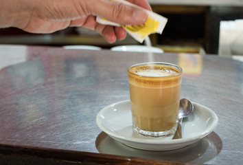 Male hand pouring sugar on a coffee.