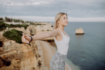 Beautiful young woman with arms raised enjoying the view on the coastline.