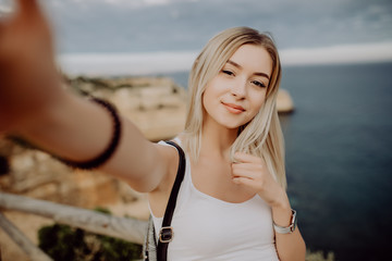 Beauty young woman take selfie from phone at the top of beautiful cliffs and rocks of Atlantic ocean in Portugal. Travel