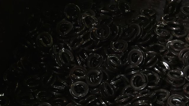 Production of steel screws in the factory ferrous metals. Hot red and orange nuts fall from the top to the container. Closeup