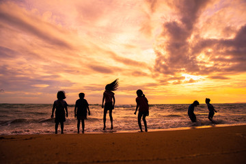 Silhouette children group enjoy playing sea waves on the beach in sunset with beautiful twilight sky