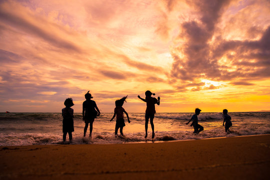 Silhouette children group enjoy playing sea waves on the beach in sunset with beautiful twilight sky