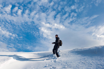 Fototapeta na wymiar A man walks on the first snow, goes uphill in the snow against a dramatic winter sunset