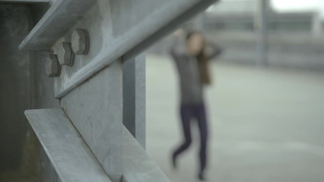 Hip hop girl walks by, putting her hood on. Focus is set on concrete elements in front