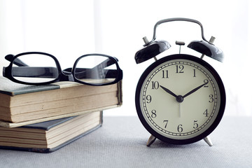 An alarm clock, spectacles and books over white curtain background