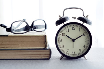 An alarm clock, spectacles and books over white curtain background