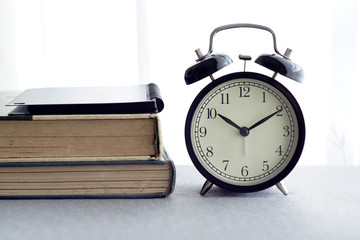 An alarm clock, spectacles and books over white curtain background