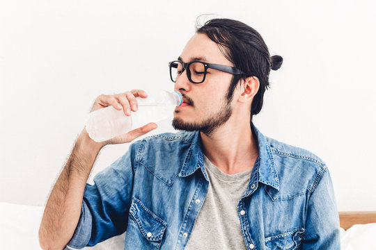 Healthy young man drinking water from a bottle  while relaxing and feeling fresh at home