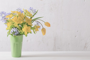 yellow and blue flowers in vase on background old white wall